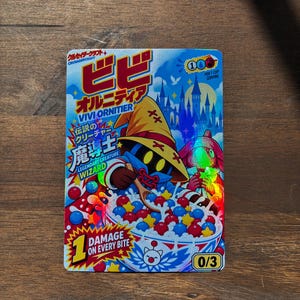 May include: A rectangular trading card featuring a holographic illustration of a wizard character eating a bowl of colorful star and sphere cereal. The card includes text such as Vivi Ornitier, Legendary Creature, and 1 Damage on every bite.