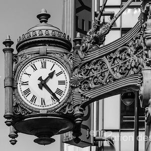 Könnte beinhalten: Ein Schwarzweißfoto eines großen, verzierten Zifferblatts mit römischen Ziffern. Die Uhr ist an einem Gebäude mit aufwendigen Details angebracht. Das Zifferblatt ist scharf, während das Gebäude unscharf ist.