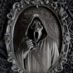 May include: A black 3D-printed wall plaque featuring a hooded figure with a ghost-like mask holding a knife, set within an ornate, oval-shaped frame. The background of the plaque displays a relief of a crescent moon, stars, and bare tree branches.