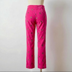 May include: Bright pink corduroy pants with a straight leg. The pants are adorned with a repeating pattern of embroidered gold-colored floral designs. The pants are displayed on a mannequin.
