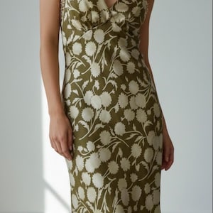 May include: Olive green floral print dress with a halter neckline and a flowing silhouette. The dress features a white floral pattern and gold sequin straps. A stylish choice for special occasions.