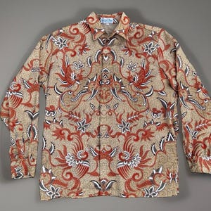 May include: A long-sleeve button-down shirt featuring a tan background with an intricate, repeating pattern of red and white phoenix-like birds, floral motifs, and swirling vine details. The shirt has a standard collar and a front button placket.