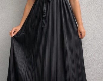 May include: A floor-length black dress with a pleated skirt and spaghetti straps. The dress features a fitted bodice and a matching tie belt at the waist. The model is wearing black sandals.