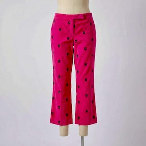 May include: Bright pink corduroy pants with black embroidered floral details. The pants have a classic fit with a slight flare at the hem. The pants are displayed on a mannequin.