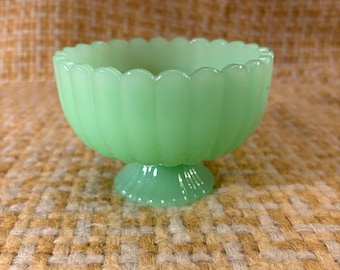Könnte beinhalten: Eine hellgrüne Glasschale mit gewelltem Rand und einem gerippten, gefluteten Außendesign. Die Schale verfügt über einen Standfuß und ist aus durchscheinendem Glas im Jadeit-Stil gefertigt, das eine glatte, glänzende Oberfläche aufweist.