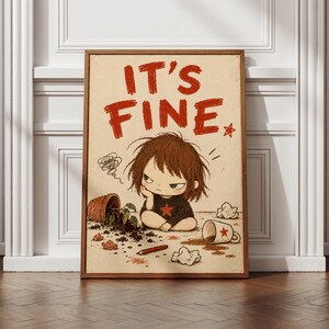 May include: A framed wall art print featuring the text IT'S FINE in red letters above a cartoon illustration of a child with messy brown hair wearing a black shirt with a red star, sitting near a spilled plant pot and a tipped coffee mug.