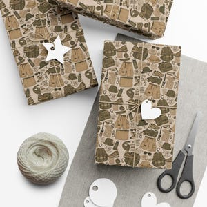 May include: Wrapping paper featuring a repeating pattern of hiking gear including backpacks, cargo shorts, hiking boots, water bottles, and hats in shades of brown and olive green. The paper is tied with twine and white star and heart-shaped gift tags.