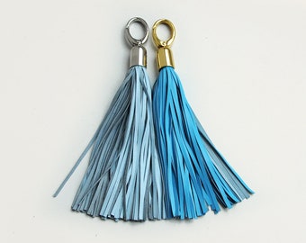 May include: Two leather tassels with metal rings. The tassel on the left is pale blue and the tassel on the right is sky blue.