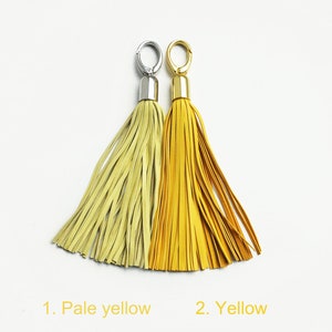 May include: Two leather tassels with gold and silver metal rings. The tassel on the left is pale yellow and the tassel on the right is yellow.