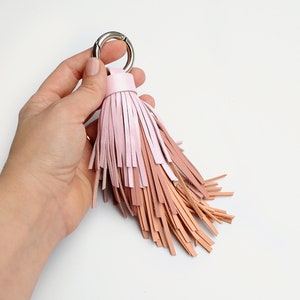 Puede incluir: Un llavero de borla de cuero rosa y marrón con un anillo plateado.