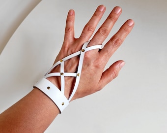 May include: White leather fingerless glove with a criss-cross design and gold-toned metal accents.