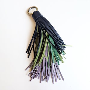Op de afbeelding: Een sleutelhanger met een leren kwast in verschillende kleuren. De kwast heeft een donkerblauwe bovenkant met groene, lavendelkleurige en zwarte leren stroken. Een stijlvol accessoire.