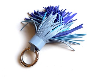 May include: A blue leather tassel keychain with a silver ring. The tassel is made of multiple shades of blue leather strips.