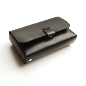 May include: A black leather clutch with a flap closure and a silver buckle. The clutch has a smooth, textured surface and is accented with silver rivets.
