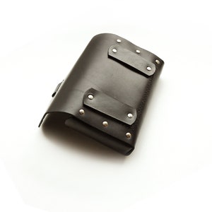 May include: A black leather tool pouch with silver metal rivets and a flap closure.