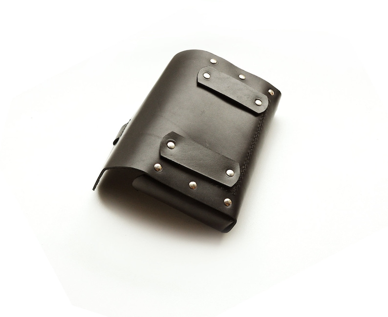 May include: A black leather tool pouch with silver metal rivets and a flap closure.
