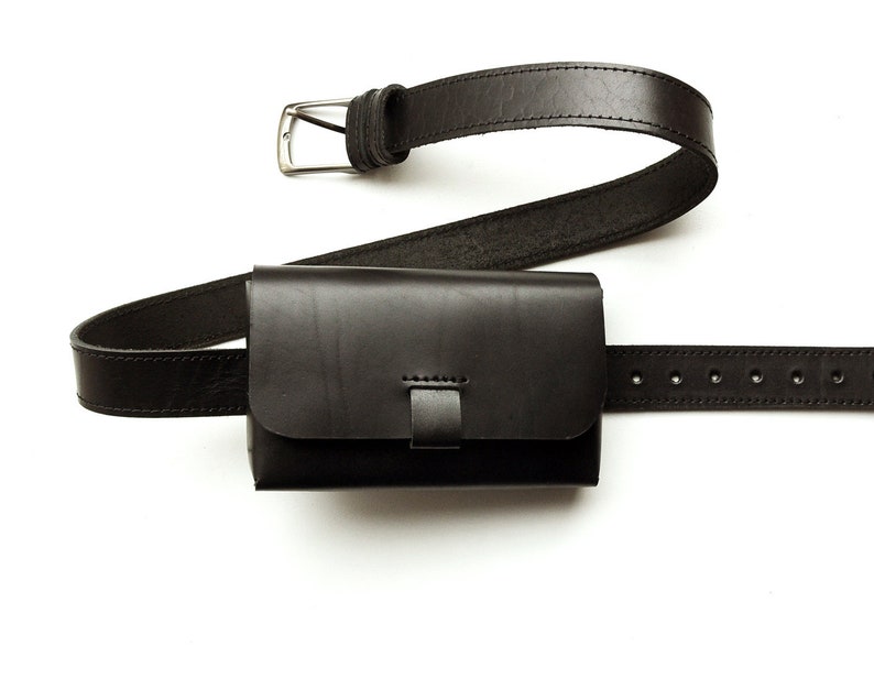 May include: A black leather fanny pack with a buckle closure. The pack is attached to a black leather belt with a silver buckle.