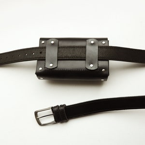 May include: Black leather belt with a black leather pouch attached. The pouch has silver rivets and a black strap. The belt has a silver buckle.