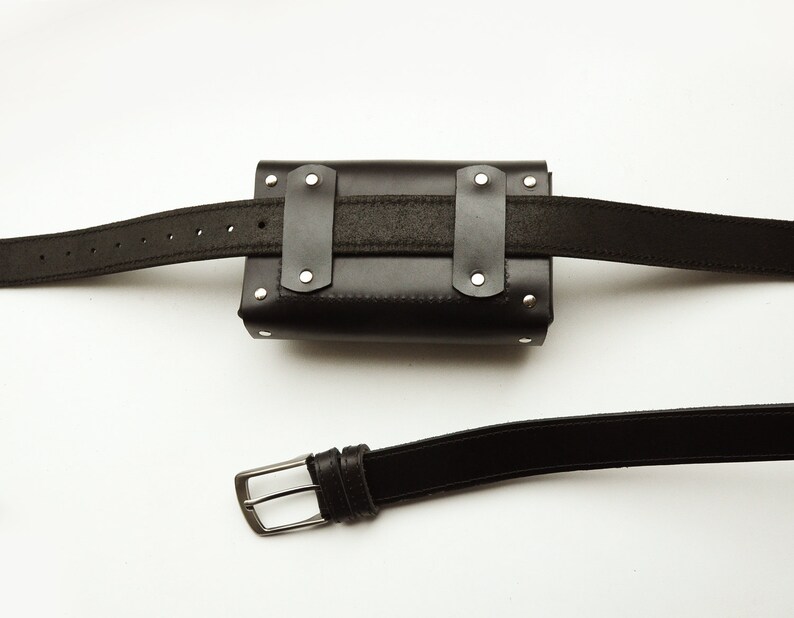 May include: Black leather belt with a black leather pouch attached. The pouch has silver rivets and a black strap. The belt has a silver buckle.