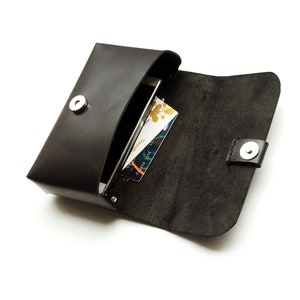 May include: A black leather phone case with a snap closure. The case is open and a smartphone and credit cards are inside.