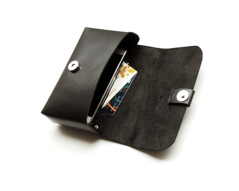 May include: A black leather phone case with a snap closure. The case is open and a smartphone and credit cards are inside.