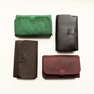 May include: Four leather wallets in different colors: green, brown, black, and burgundy. Each wallet has a flap closure with a stitched strap.