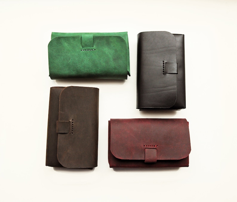 May include: Four leather wallets in different colors: green, brown, black, and burgundy. Each wallet has a flap closure with a stitched strap.