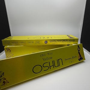 Puede incluir: Dos cajas rectangulares amarillas de varitas de incienso Ohli-Way Yellow OSHUN 7 in 1. El empaque presenta texto negro, patrones florales decorativos y una ilustración de una figura con vestido amarillo. Fabricado por Charu Perfumery House.