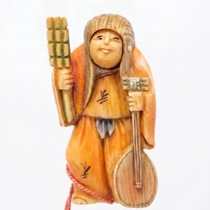 May include: A carved netsuke figurine depicting a smiling figure with long hair, wearing an orange robe. The figure holds a rectangular grid-like object in the right hand and a round stringed instrument in the left hand, with a red cord attached.