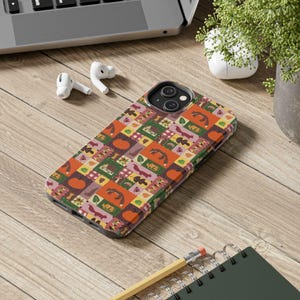 May include: A smartphone case featuring a repeating patchwork pattern of autumn-themed illustrations including orange pumpkins, red foxes, green leaves, small houses, and plaid squares in shades of orange, green, brown, and pink on a dark background.
