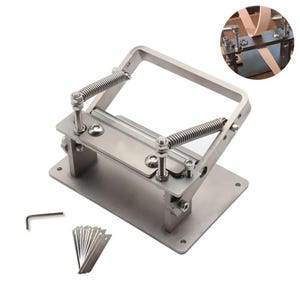 May include: A silver-toned metal leather skiving machine featuring a rectangular base, a spring-loaded tension mechanism, and a blade holder. The set includes a small L-shaped hex key and a collection of ten replacement blades for leather crafting.