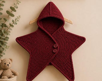 May include: A deep burgundy star-shaped hooded garment crafted from knit fabric. The piece features a pointed hood, a wide star-shaped body, and two matching circular buttons positioned on the front overlap to secure the closure.
