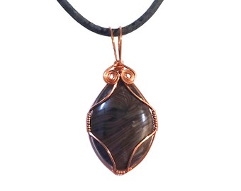 May include: A handcrafted pendant featuring a dark, striped stone encased in copper wire. The stone is teardrop-shaped and suspended from a black cord. The copper wire is intricately wrapped around the stone, creating a unique, artistic design.
