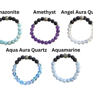 May include: Five gemstone bracelets are displayed, each with a different stone and color. The bracelets include Amazonite, Amethyst, Angel Aura Quartz, Aqua Aura Quartz, and Aquamarine. Each bracelet has black lava beads and a silver-colored accent bead.