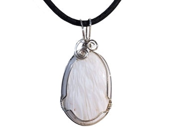 May include: A white oval pendant with a feathery texture, encased in a silver wire frame, hangs from a black cord. The pendant's design features a swirling wire detail at the top. The jewelry is set against a white background.