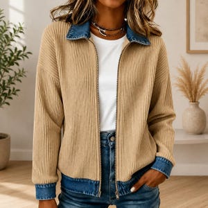 May include: A beige ribbed zip-up jacket featuring a blue denim collar and matching blue denim cuffs at the wrists and hem. The jacket is worn over a plain white t-shirt and is paired with blue denim jeans, showcasing a layered texture design.