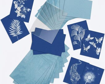 Op de afbeelding: Een verzameling rechthoekige kaarten en doorzichtige plastic vellen. De kaarten hebben diepblauwe achtergronden met witte lijntekeningen van bloemen, een palmblad, vlinders, een tijger en paardenbloemen, naast effen lichtblauwe kaarten.