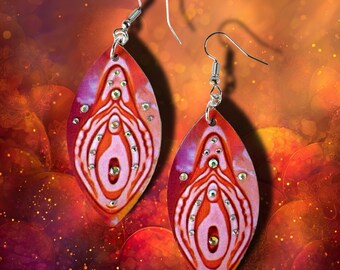 May include: A pair of leaf-shaped dangle earrings featuring a vibrant red, orange, and pink marbled pattern. Each earring is adorned with small, clear, sparkling rhinestones arranged in a symmetrical design and attached to silver-toned metal hooks.