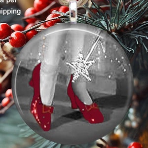 May include: A large Christmas ornament, 2.25 inches across, features a black and white image of red shoes and a star. The ornament hangs from a jute string and is surrounded by Christmas tree branches and red berries.