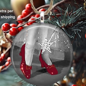 May include: A round Christmas ornament measuring 2.25 inches across, featuring a black and white image of feet wearing red shoes and a star-shaped wand. The ornament has a silver-toned metal bail and is suspended by a natural jute twine loop.