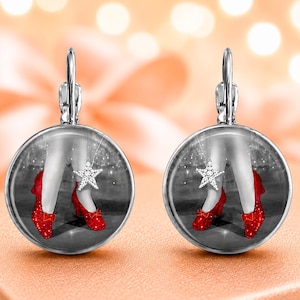 May include: A pair of round stainless steel earrings featuring a black and white image of legs wearing bright red slippers and a silver star pendant. The text above the earrings reads: Oz ruby slippers stainless earrings, choice of style & size.