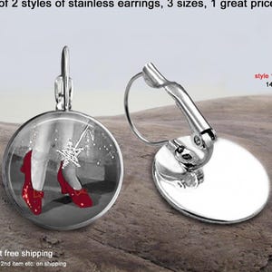 May include: Two stainless steel leverback earrings. One earring features a circular graphic of red shoes and a star wand on a grayscale background. The other earring is plain silver. Text reads: choice of 2 styles of stainless earrings, 3 sizes, 1 great price, style 1 leverback 14 or 16mm, spend $35 get free shipping.