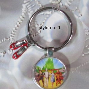 May include: Silver-tone keychain featuring a round pendant with a scene from The Wizard of Oz and a charm of red ruby slippers. The keychain also has the text "style no. 1".
