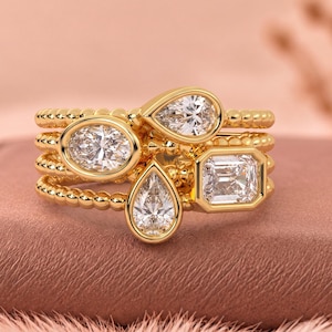 Peut inclure: Une bague en or au design empilé avec une texture perlée. La bague est ornée de quatre pierres précieuses transparentes et facettées de formes variées, dont deux poires, une ovale et une émeraude rectangulaire, toutes serties clos.