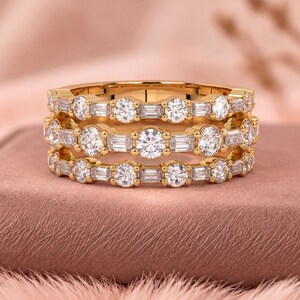 Può includere: Un anello in oro composto da tre fasce parallele collegate tra loro. Ogni fascia è incastonata con un'alternanza di pietre rotonde taglio brillante e pietre rettangolari taglio baguette, creando un motivo scintillante continuo.
