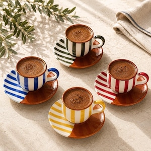 May include: Four ceramic espresso cups and saucers filled with dark coffee. Each cup features vertical stripes in black, blue, red, or yellow, with matching striped saucers that transition into a solid terracotta-colored base.