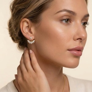 May include: A gold ear jacket earring featuring a single round brilliant-cut stone stud at the front and a fan-shaped attachment behind the earlobe, adorned with seven marquise-cut stones arranged in a curved, radiating pattern.