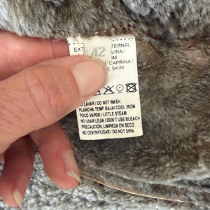 May include: A white garment care label with the number 42 printed in large font. The text includes instructions such as DO NOT WASH, COOL IRON, LITTLE STEAM, DO NOT USE BLEACH, and DO NOT SPIN. The label is attached to a textured brown faux fur lining.