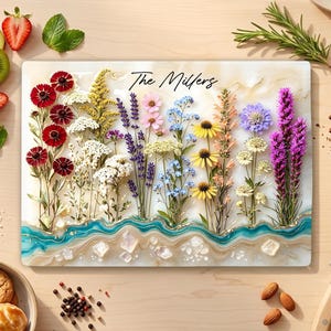 May include: A rectangular serving board featuring a pressed wildflower arrangement in red, white, yellow, blue, and purple. The text The Millers is printed at the top. The bottom edge has a wavy teal and gold resin design with clear crystal accents.