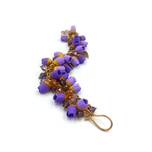 May include: A purple and gold bracelet with small flower charms and clear beads.